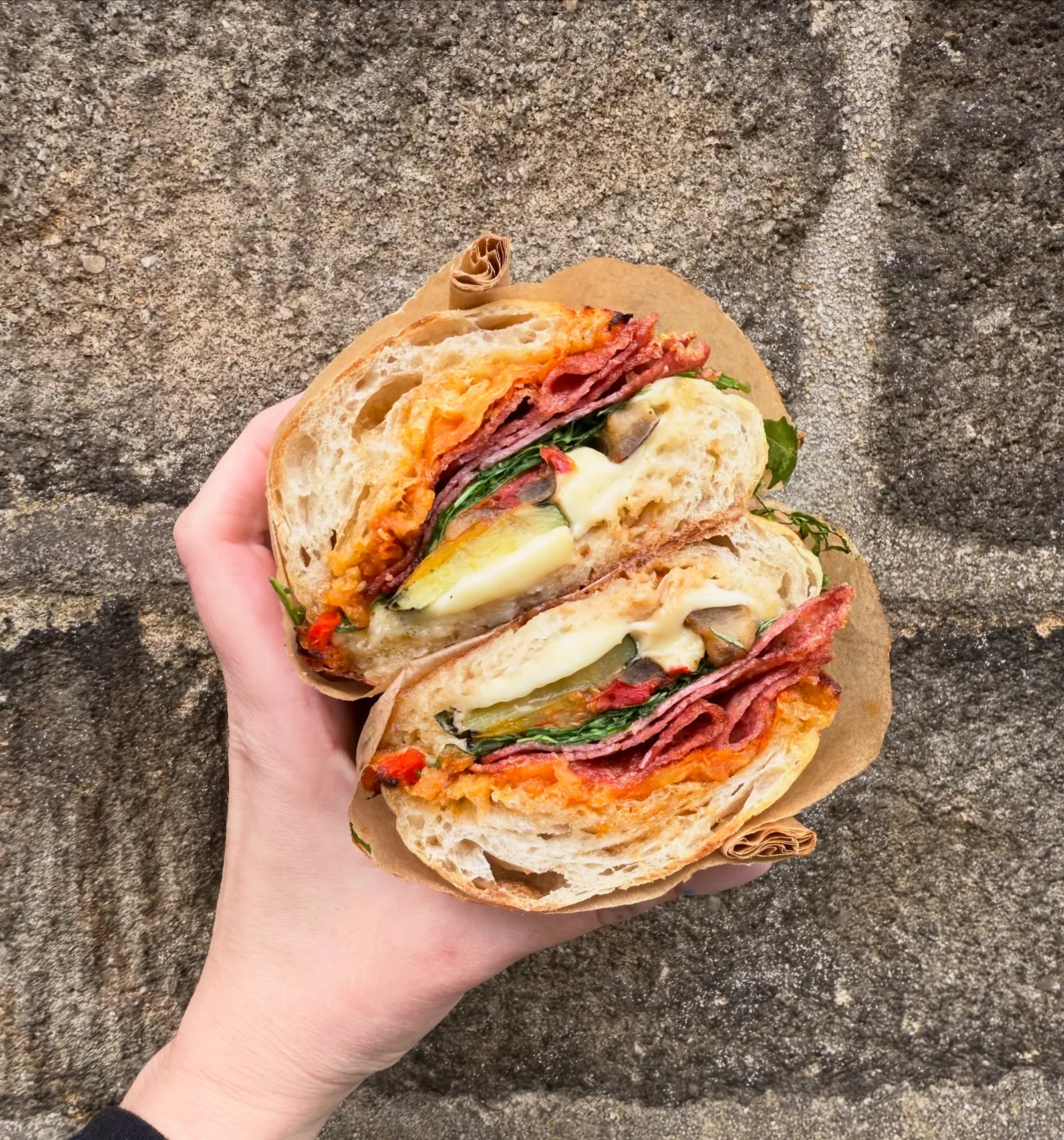 A generous filled sandwich at Arlo, held against the village stonework